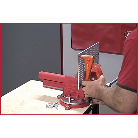 Ein Mann arbeitet mit einer Zange und einer Metallplatte, die in einem roten Schraubstock eingespannt ist.